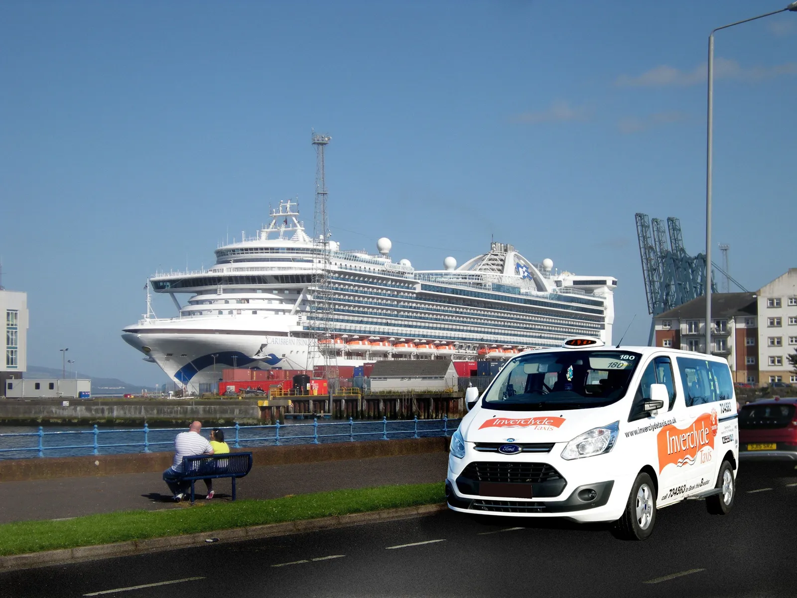 White Inverclyde Taxis van parked near a port with a large cruise ship docked in the background
