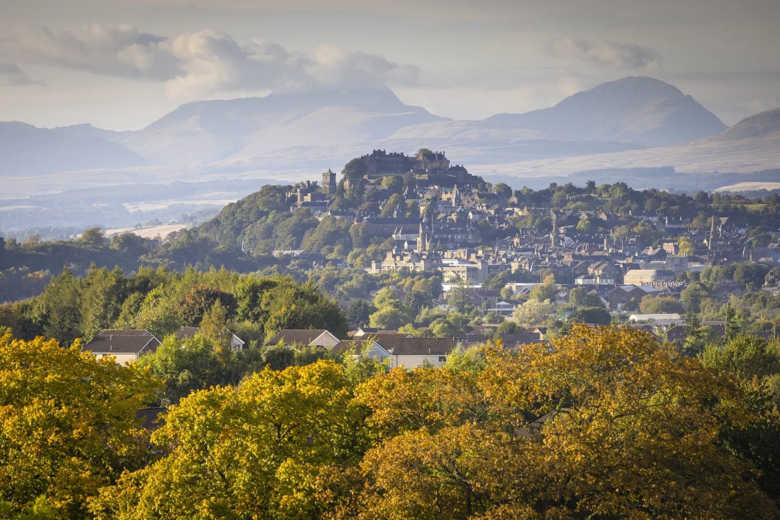 Distant landscape view of Stirling Castle atop Castle Hill with the city below and mountains rising in the background surrounded by autumn foliage