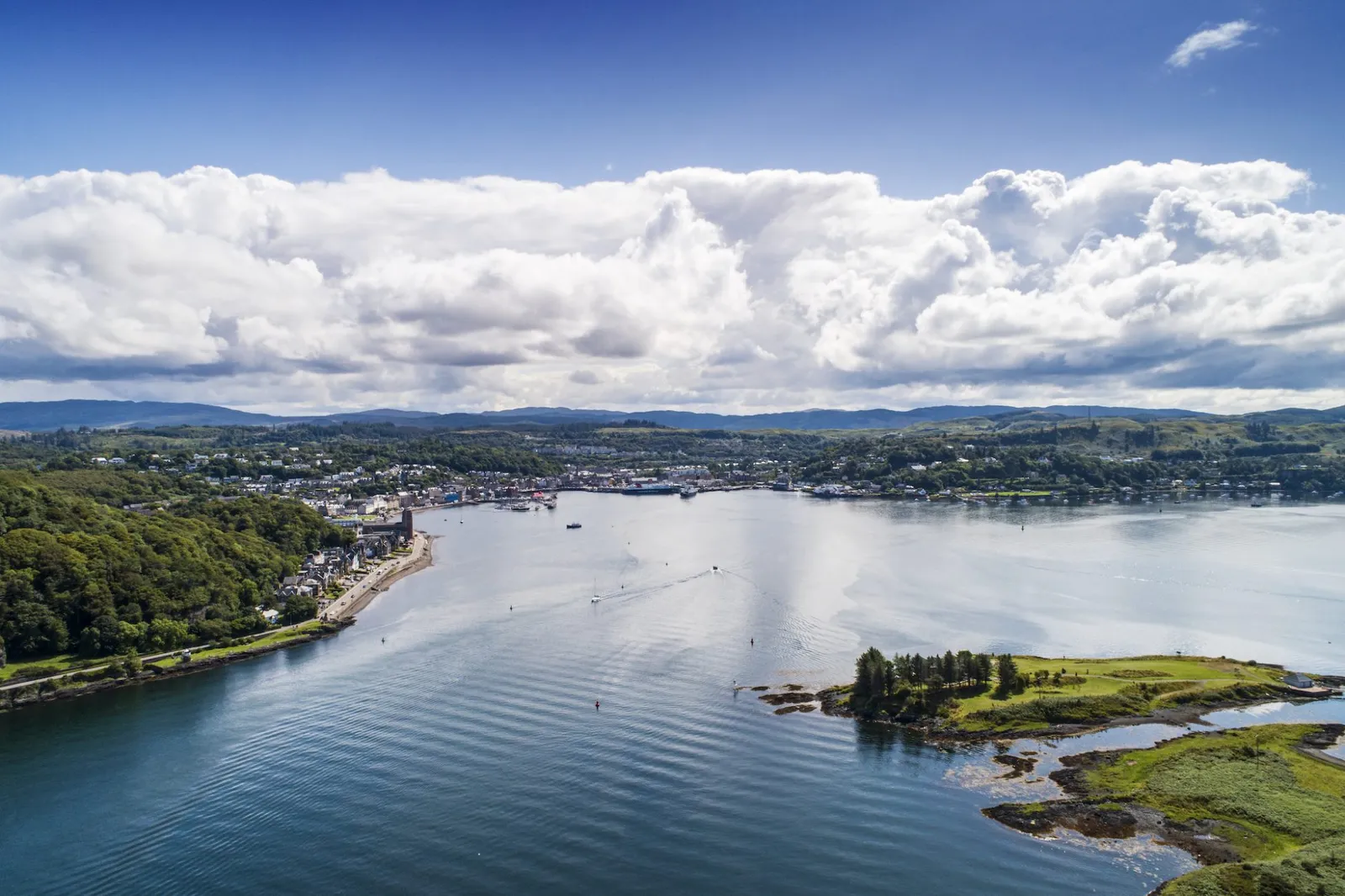 Aerial landscape view of Oban bay and town coastline under a blue sky with fluffy white clouds